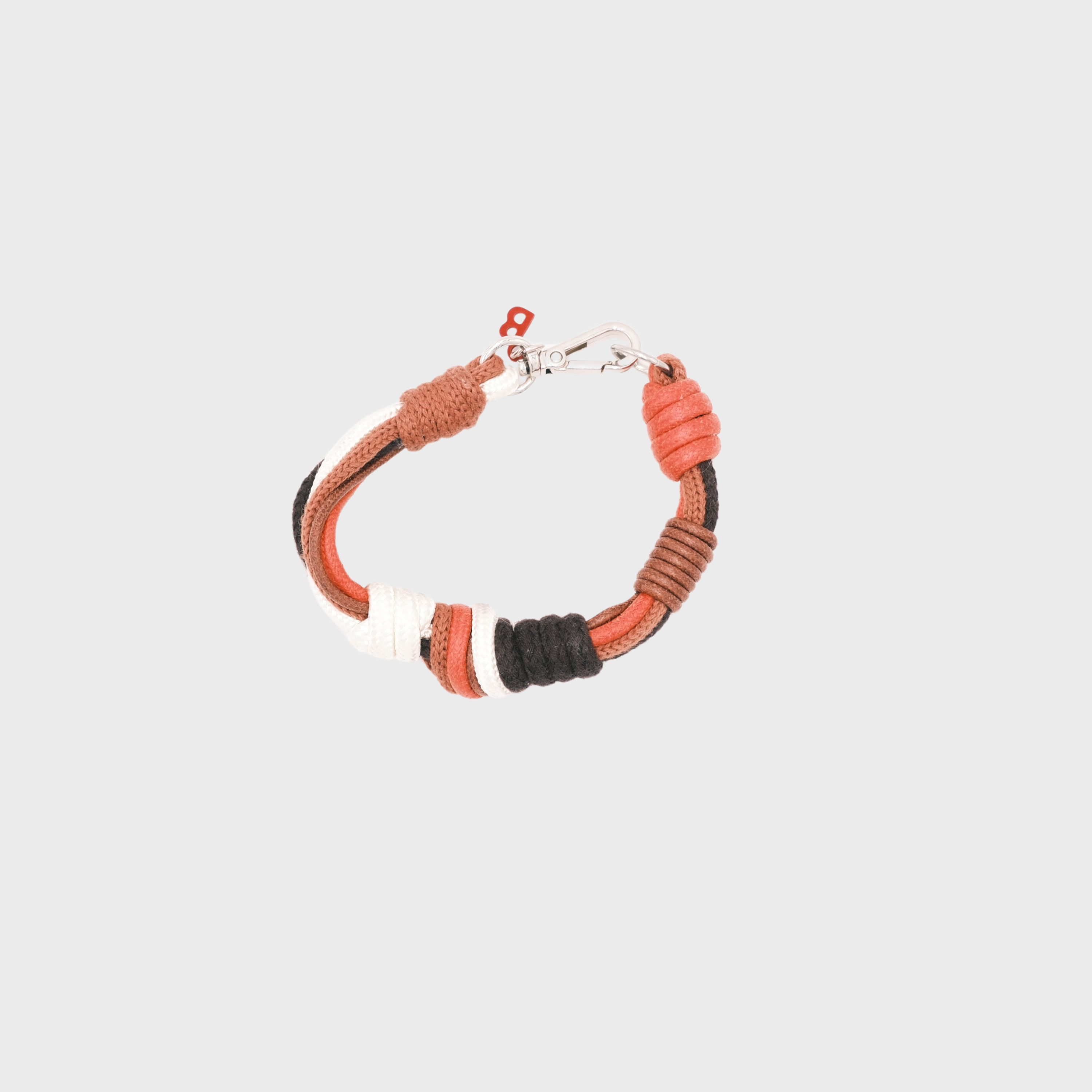 A photo taken from above of a knotted macramé bracelet in shades of red, white and brown, with a silver clasp.