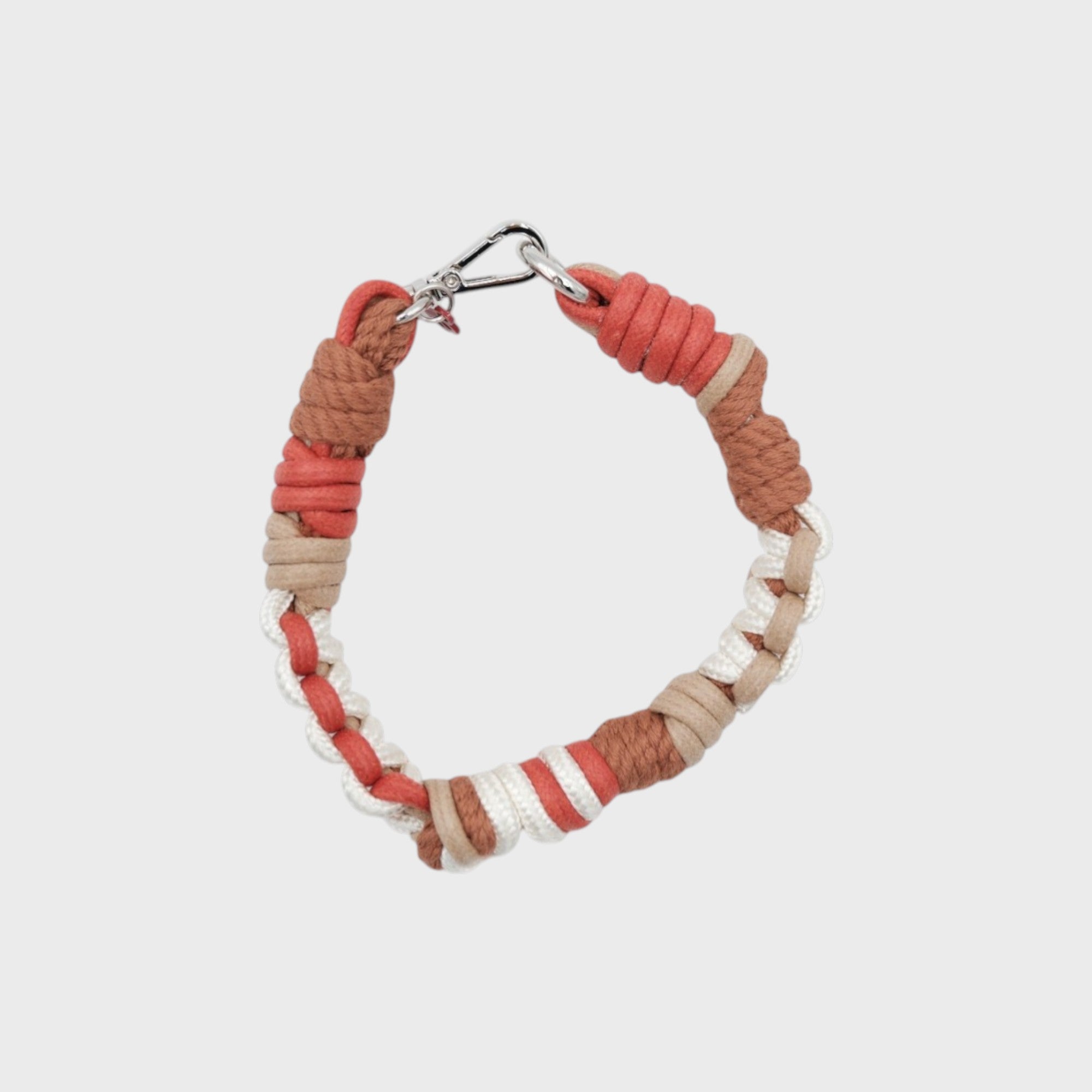 A photo taken from above of a braided macramé cord collar in shades of red, white and brown with a silver clasp.