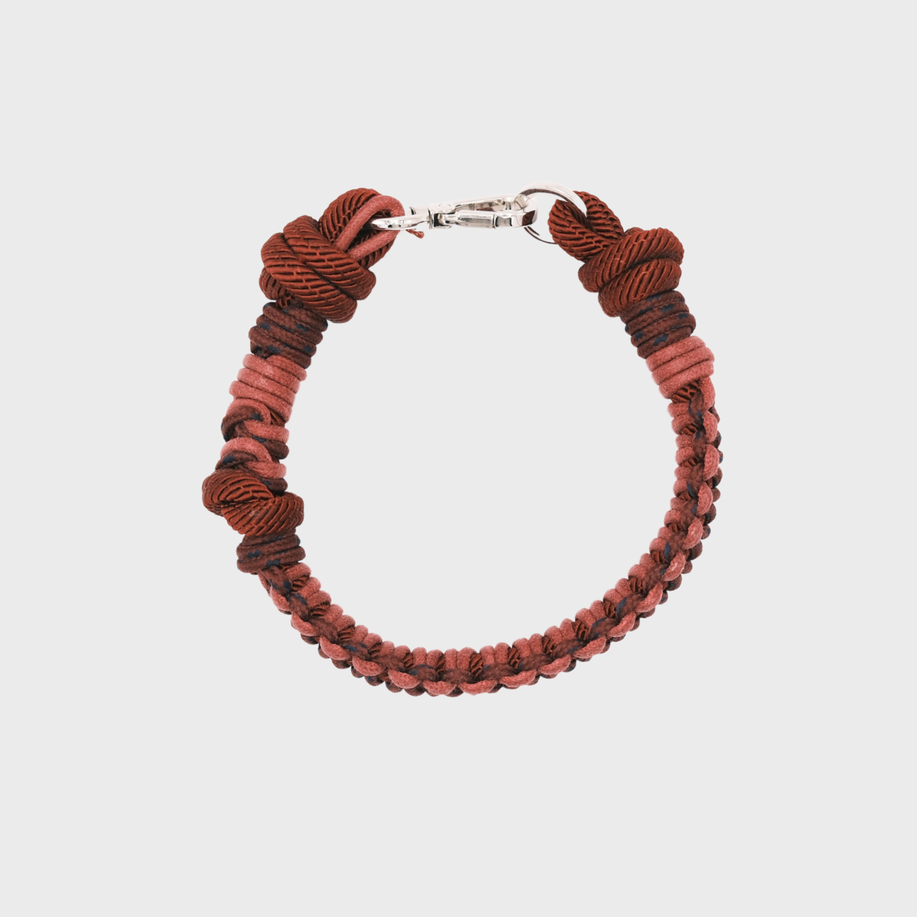 A photo taken from above of a braided macramé cord collar in shades of red and pink with a silver clasp.