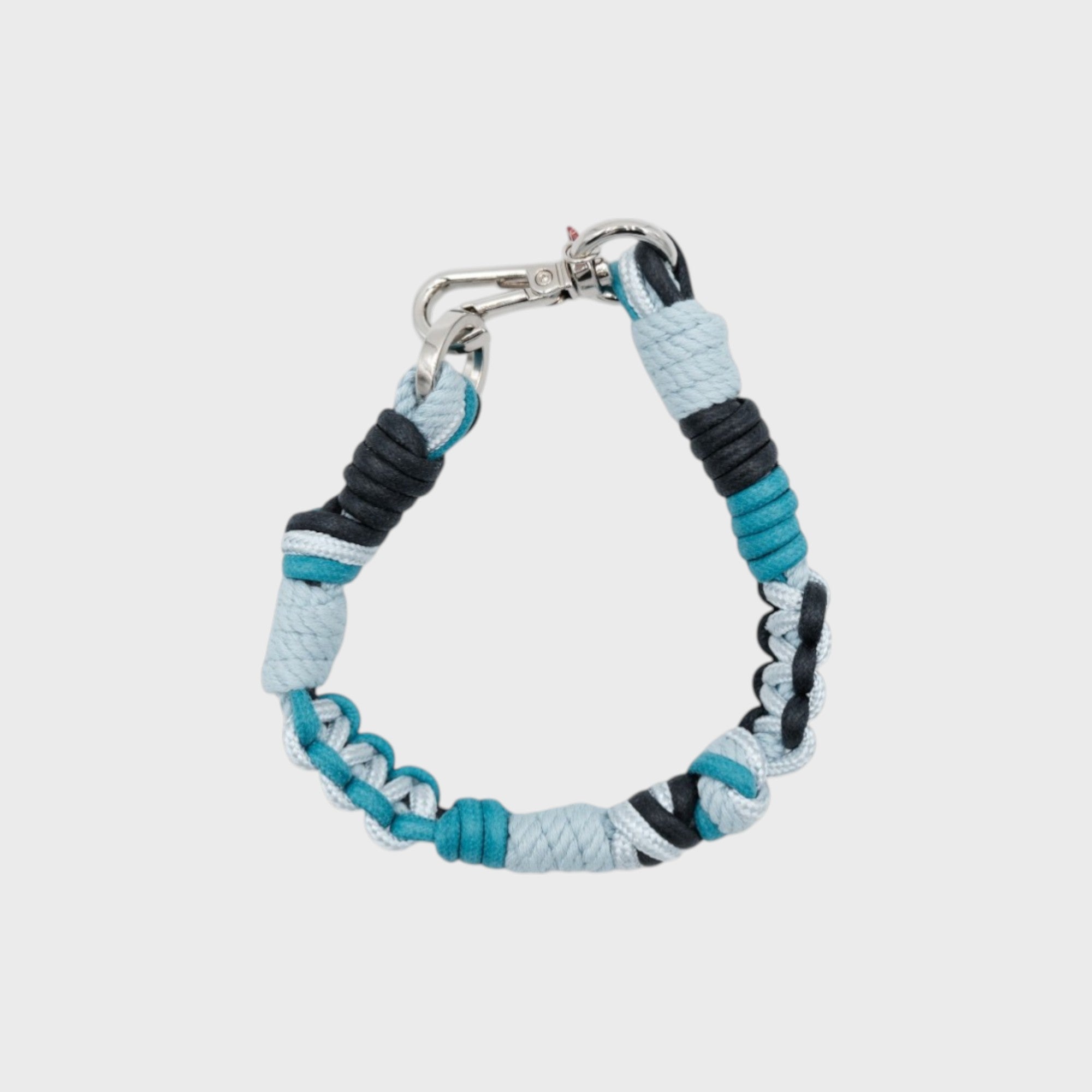 A photo taken from above of a braided macramé cord collar in shades of blue, dark blue and white with a silver clasp.