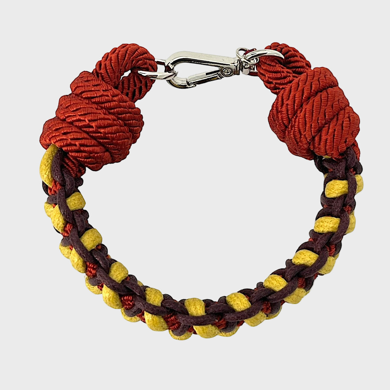 A photo taken from above of a braided macramé bracelet in shades of yellow, burgundy and red with a silver clasp.