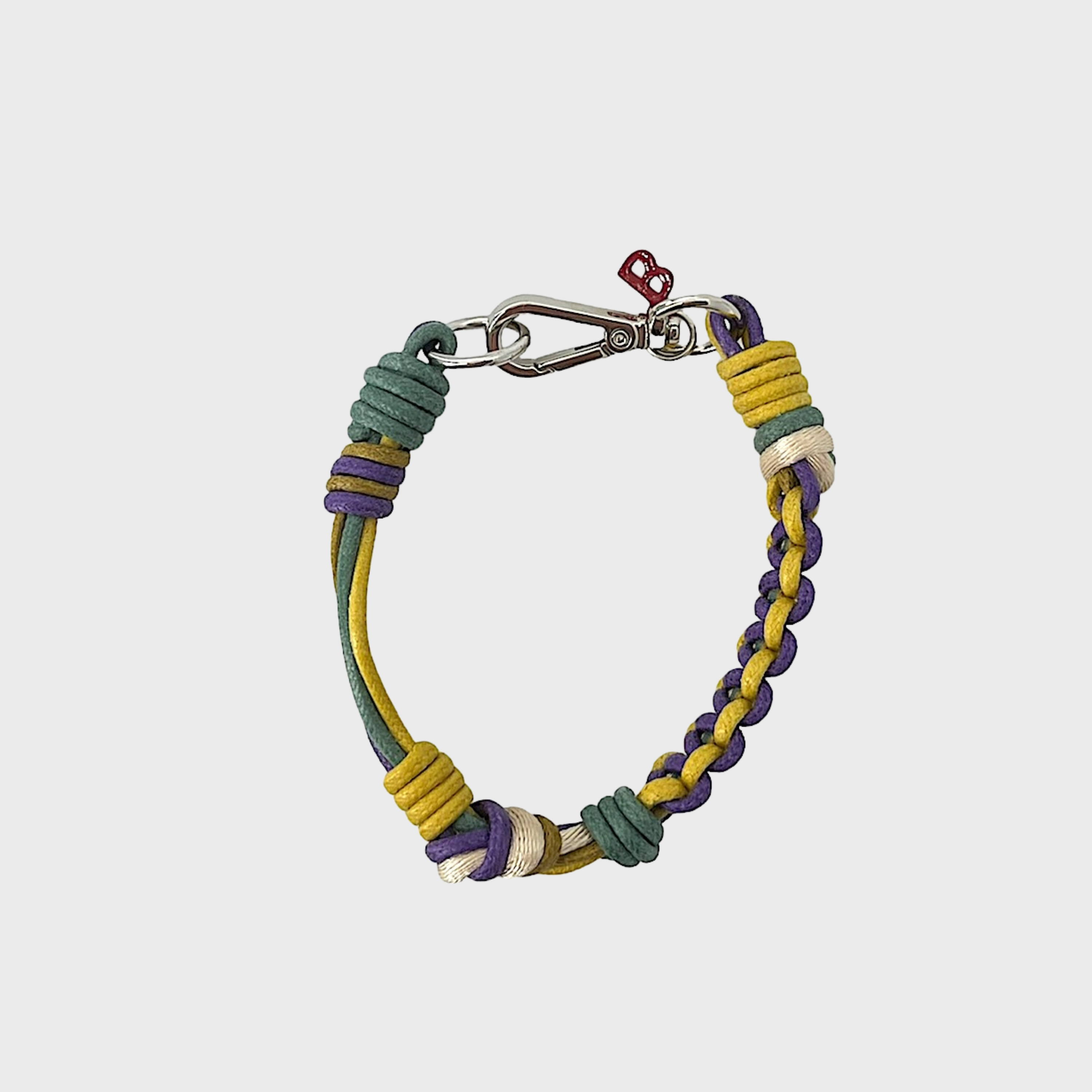 A photo taken from above of a thin braided macramé bracelet in shades of yellow, purple and green, with a silver clasp.