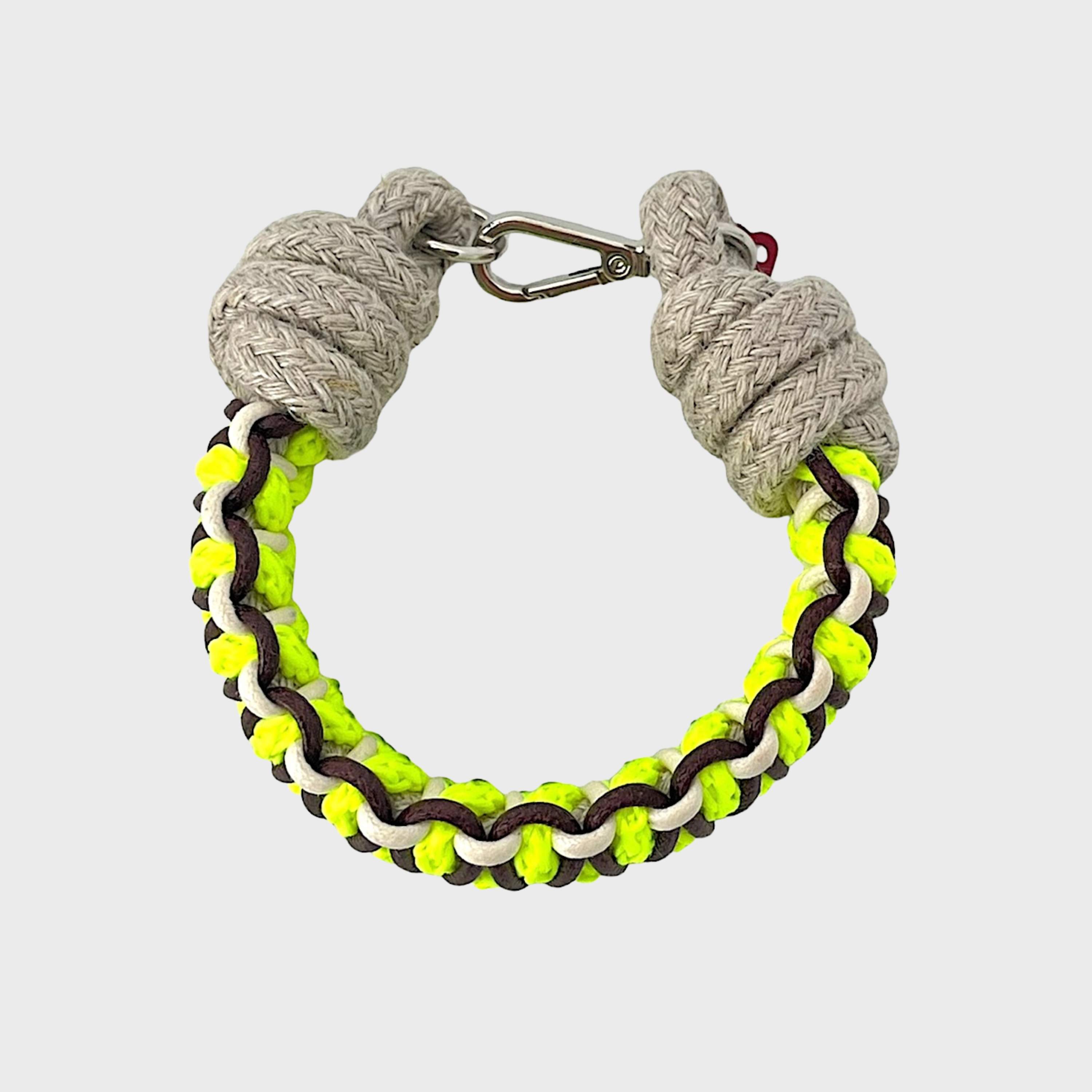 A photo taken from above of a braided macramé bracelet in shades of neon yellow, brown and beige with a silver clasp.