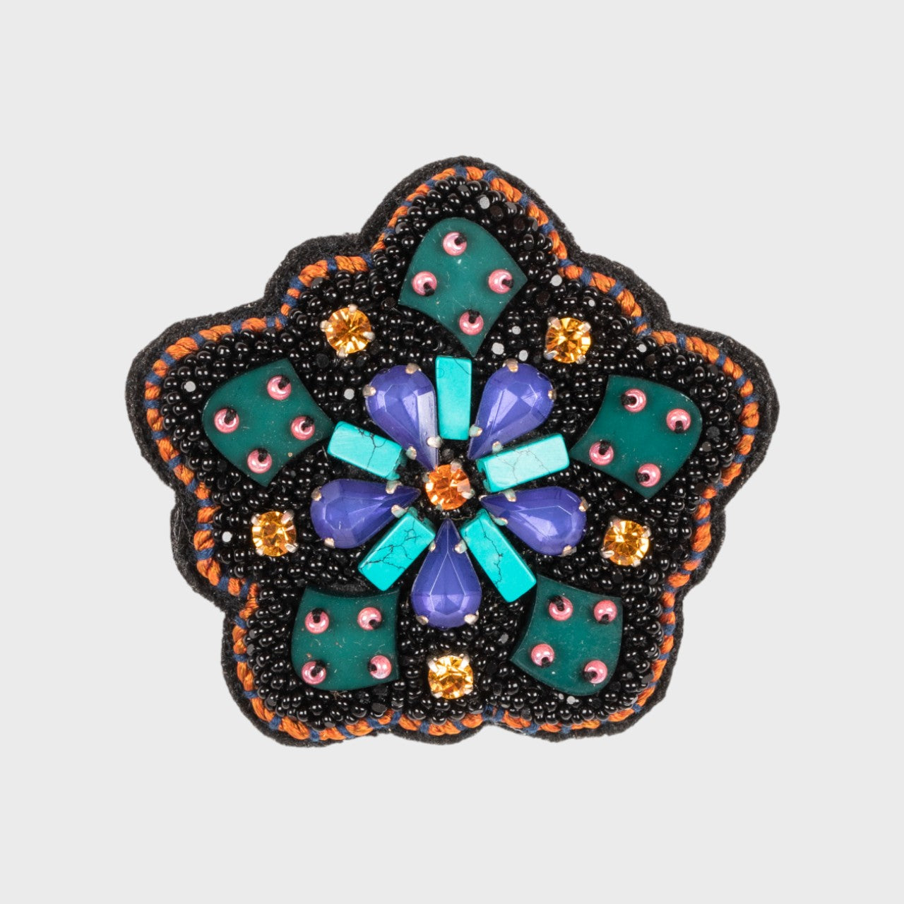 An embroidered brooch representing a wheel with green, blue, purple and orange details. 