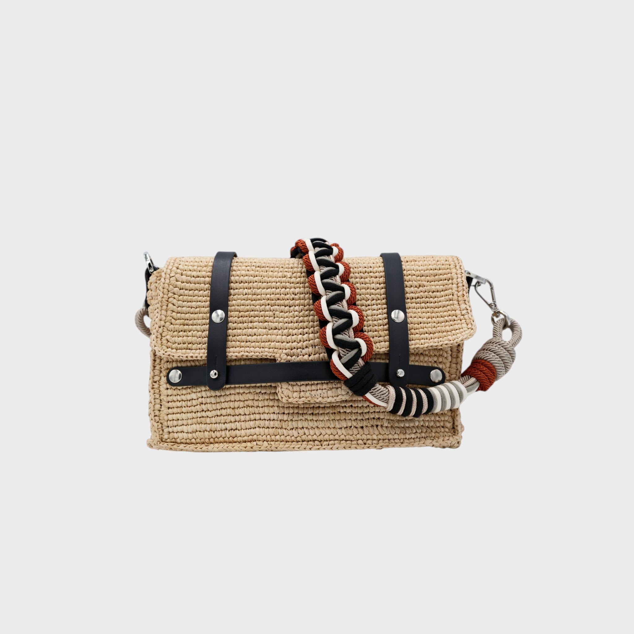A white raffia shoulder bag with black leather straps and a colorful macramé braided strap featuring grey, black and dark orange. 