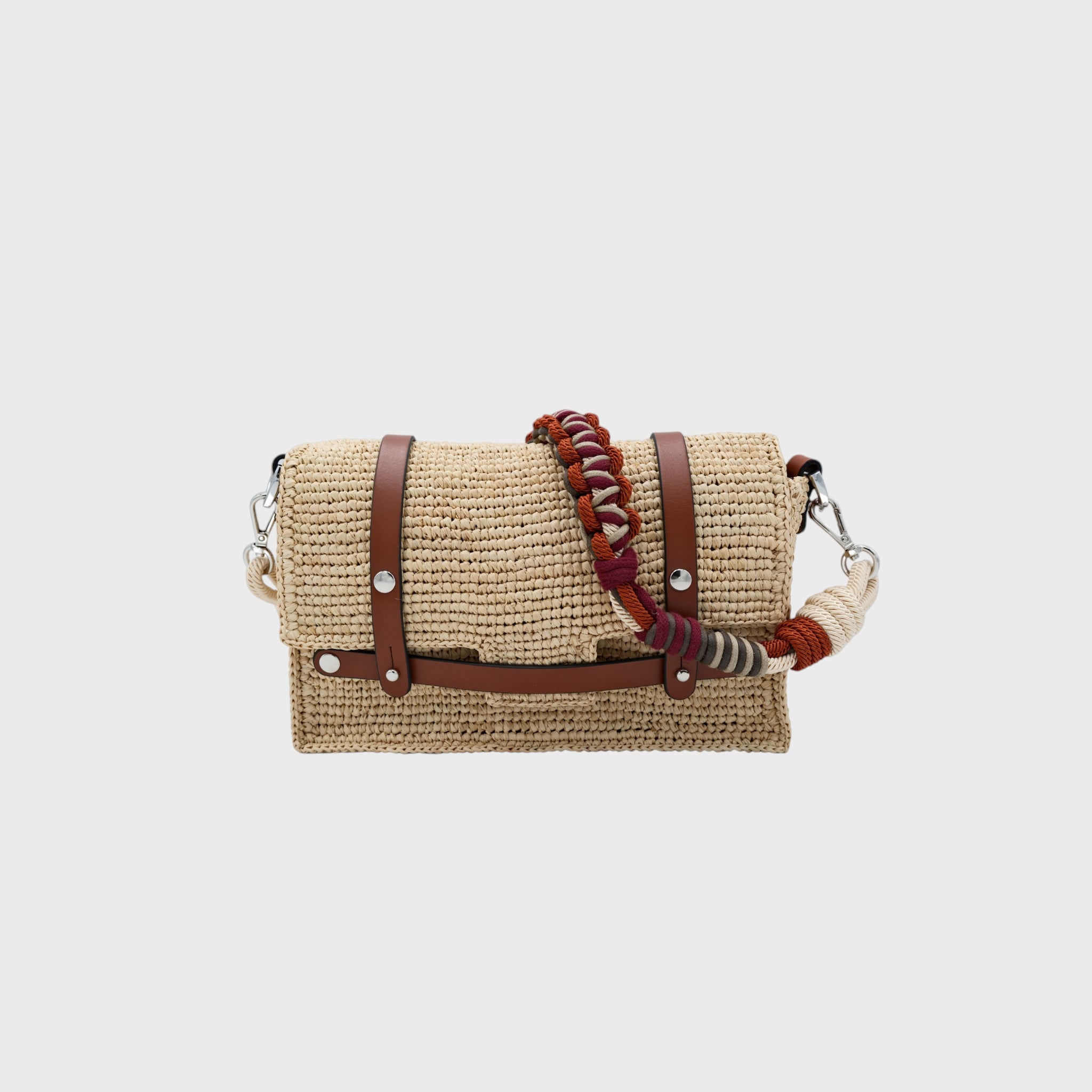 A white raffia shoulder bag with brown leather straps and a colorful macramé braided strap featuring white, burgundy and dark orange. 