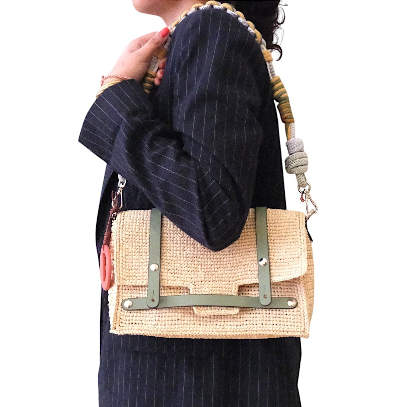 A model carrying on her shoulder the white raffia bag with green leather straps, by a yellow and light blue bag strap. 