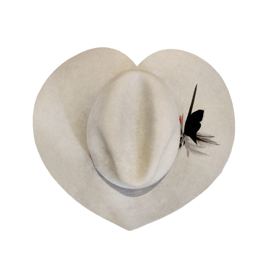 A white velvet hat shaped as a hearth taken from above with a black feather brooch. 