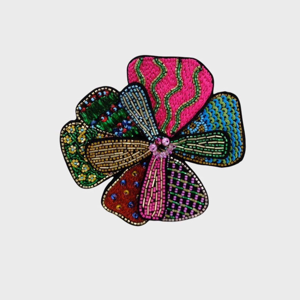 An embroidered brooch representing a windmill with green, blue an pink details. 