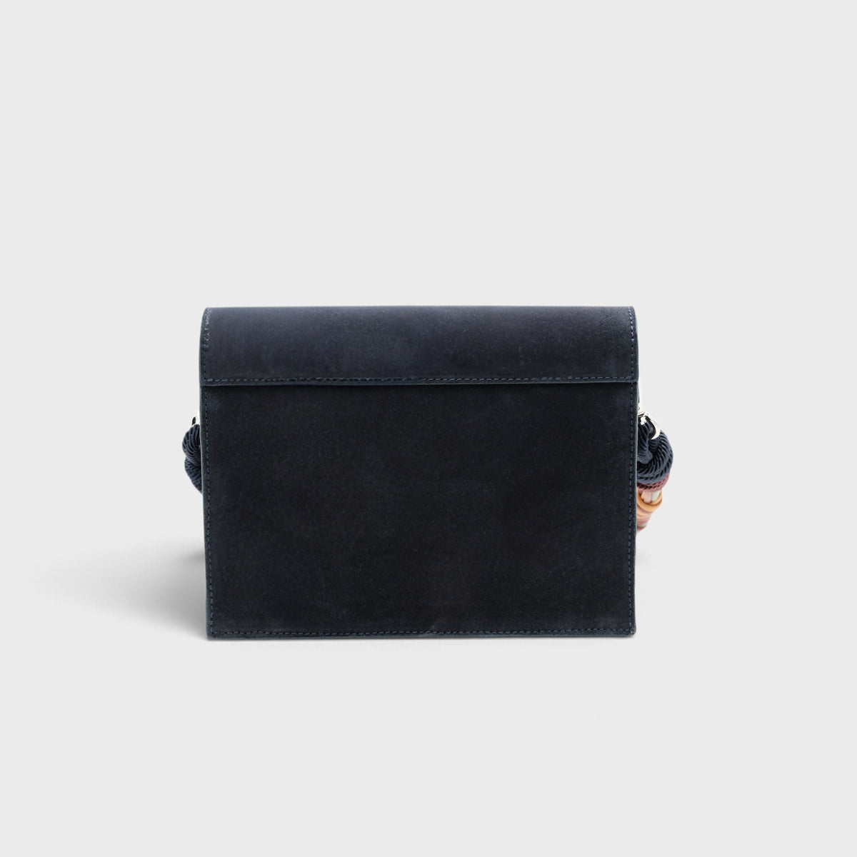The back of a rectangular suede clutch bag in a muted navy colour, shown against a solid light gray background.