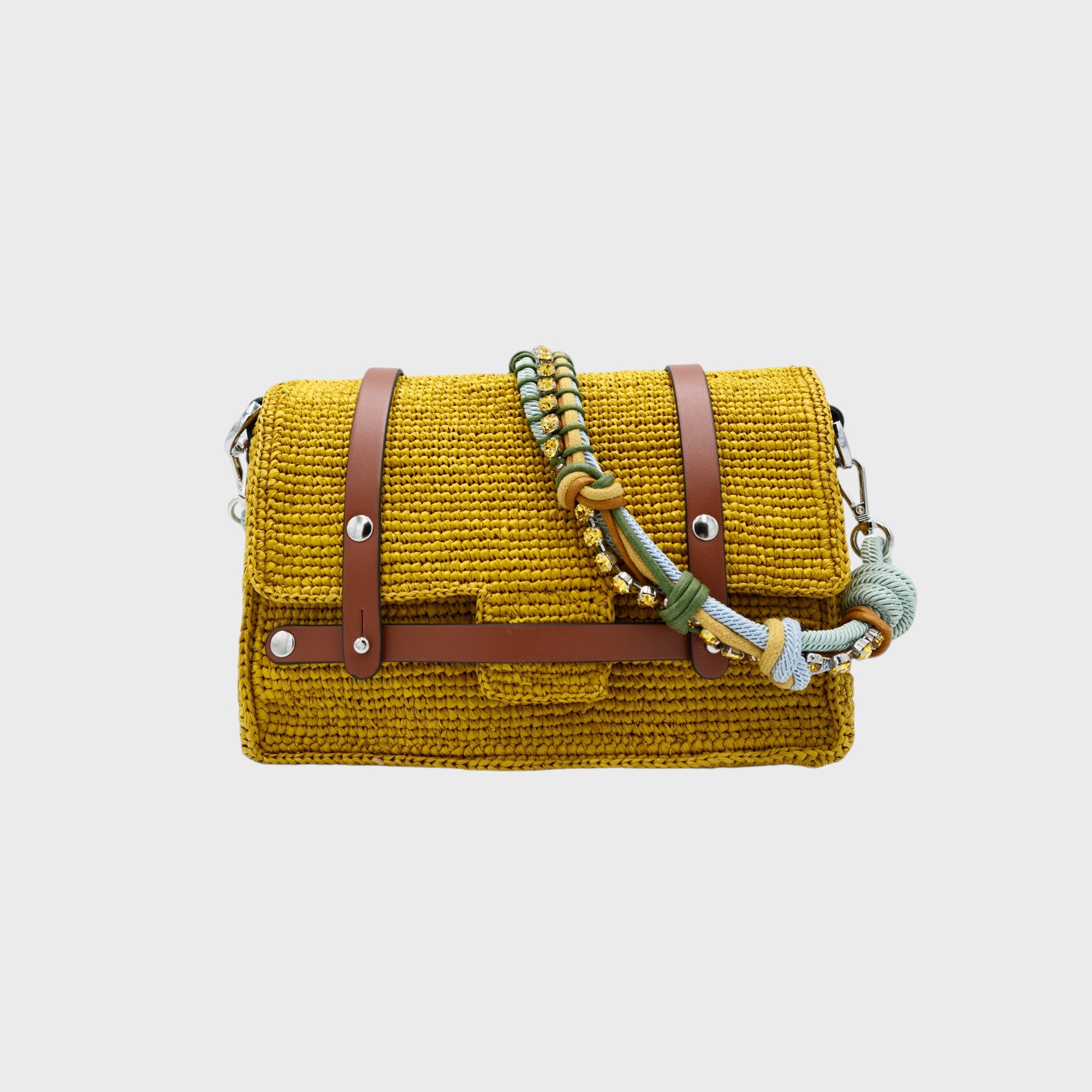 A yellow raffia shoulder bag with brown leather straps and a colorful macramé braided strap featuring green, light blue and small beaded yellow stones. 