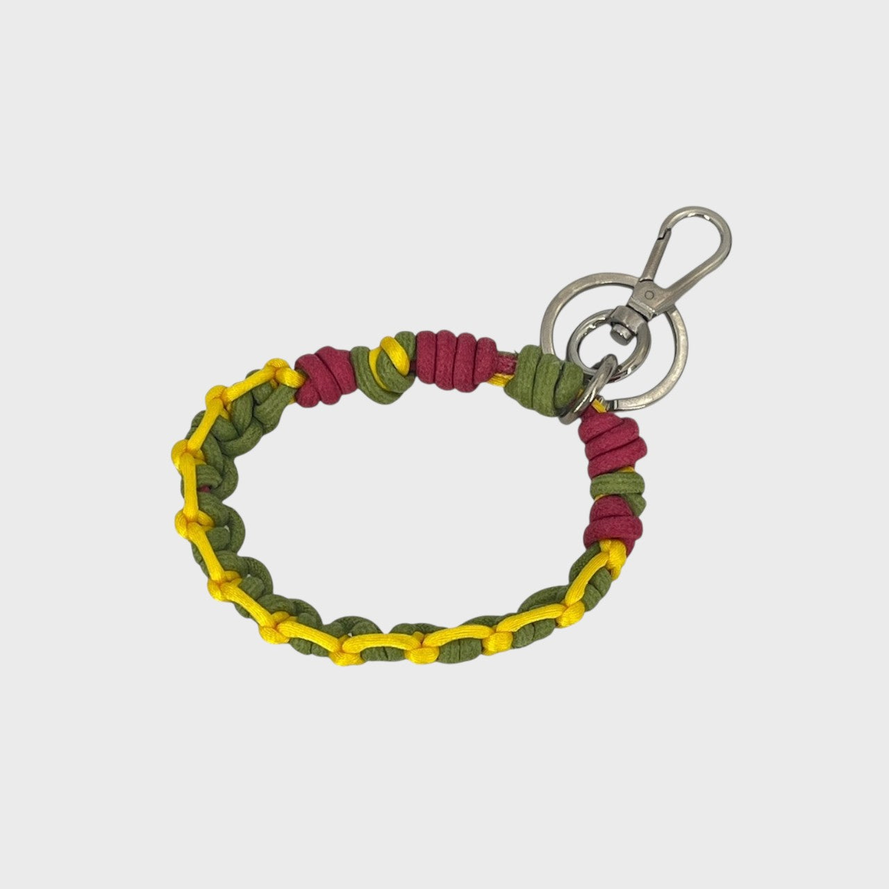 A woven macramé key chain with bright yellow, green and fuschia patterns, inspired by celtic knots, finished with silver-tone metal hardware.