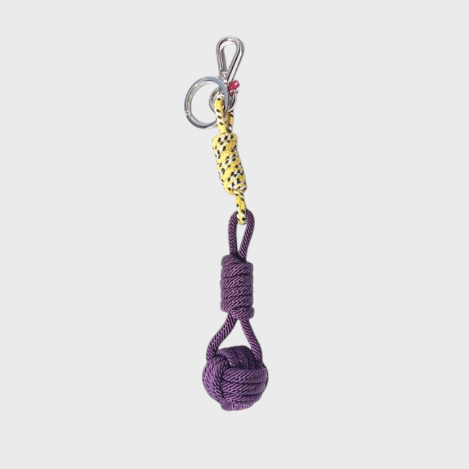 A macramé keychain representing a ball inspired by sailors knots. The straight upper part is yellow and black and the ball part is purple. 