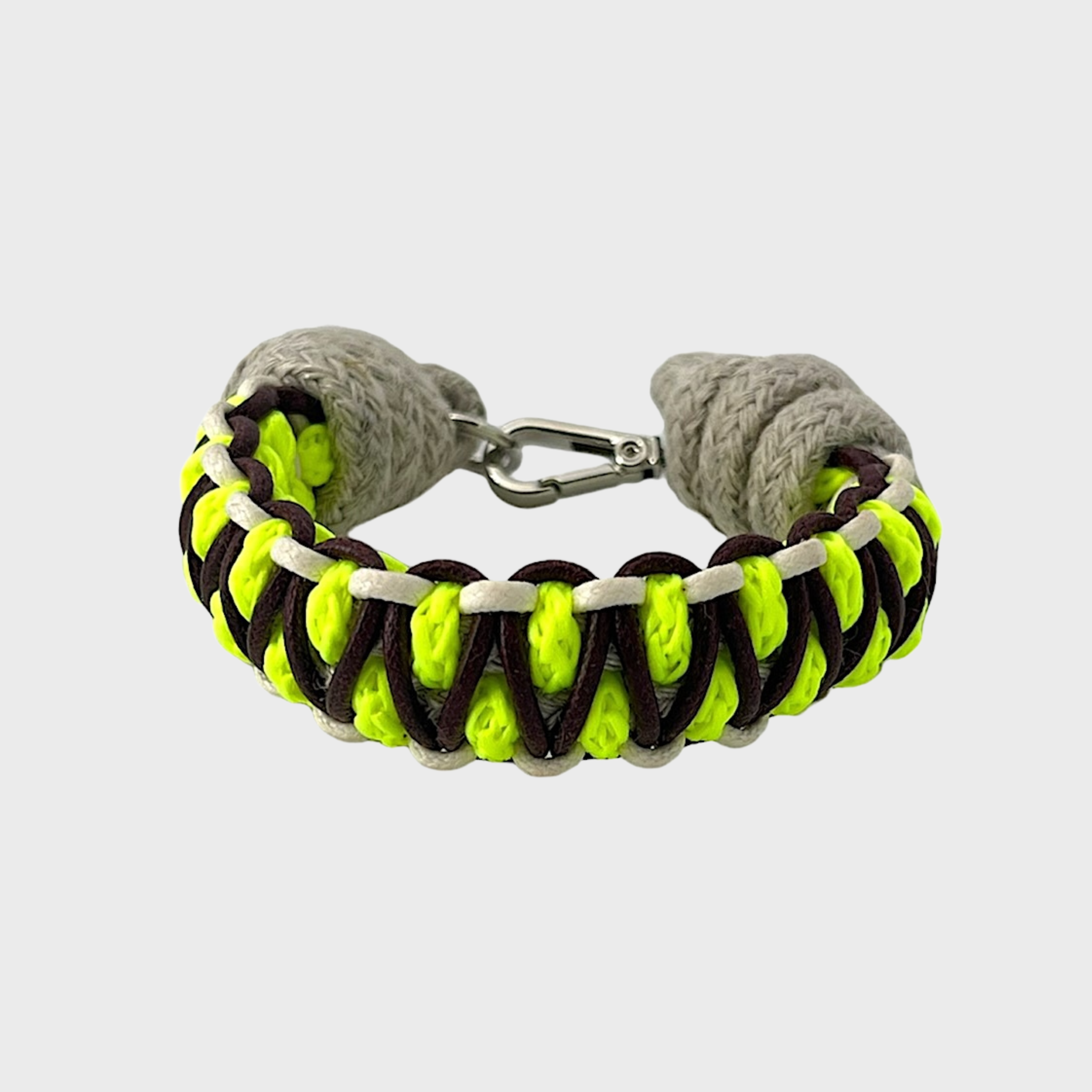 A braided macramé bracelet with shades of neon yellow, brown and beige. It ends and a silver clasp, shown on a light gray background.