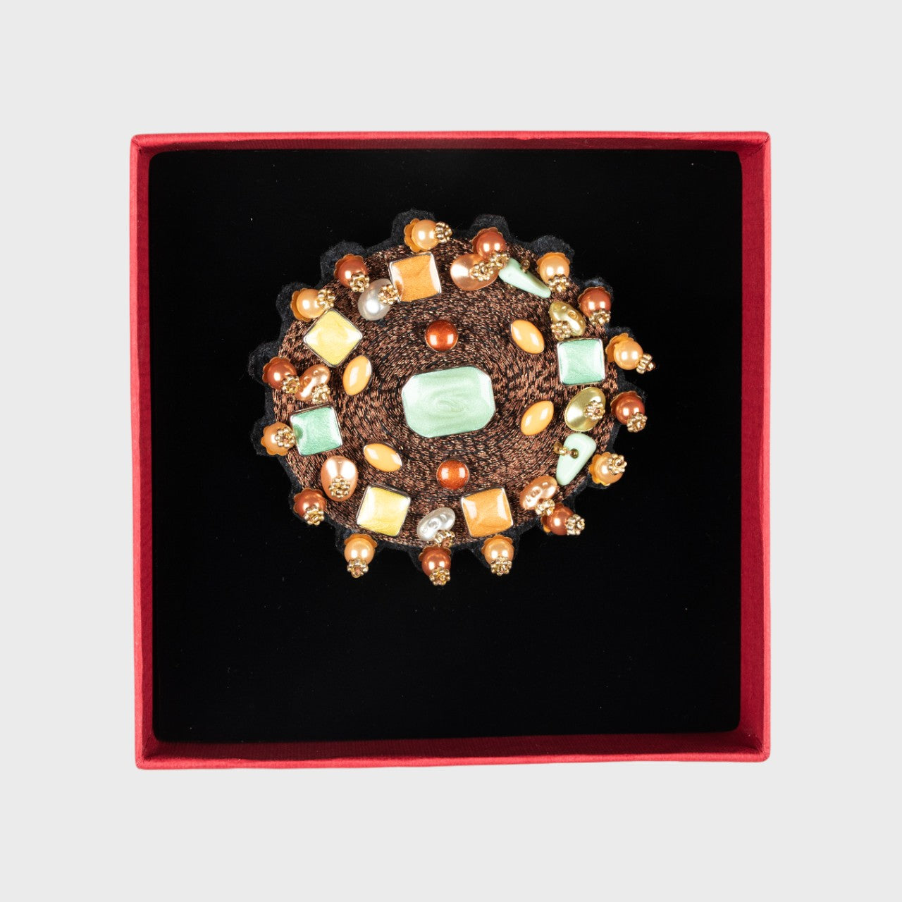An embroidered brooch representing a brown yourte in a box. 
