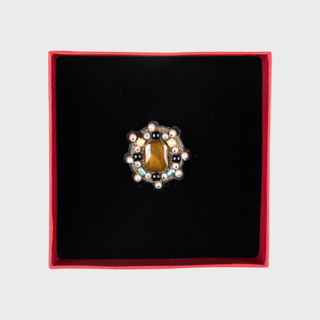 An embroidered brooch reopresenting a mini Yourte with a golden stone in a box. 