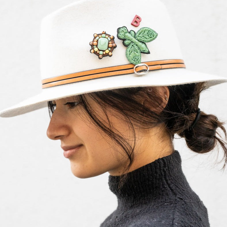 A model wearing on a hat with a small green yourte brooch. 