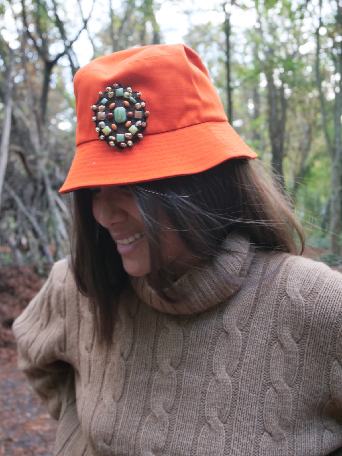 A woman wearing an orange cotton bucket hat with an embroidered brooch representing the inside of a yourte pinned on it. 