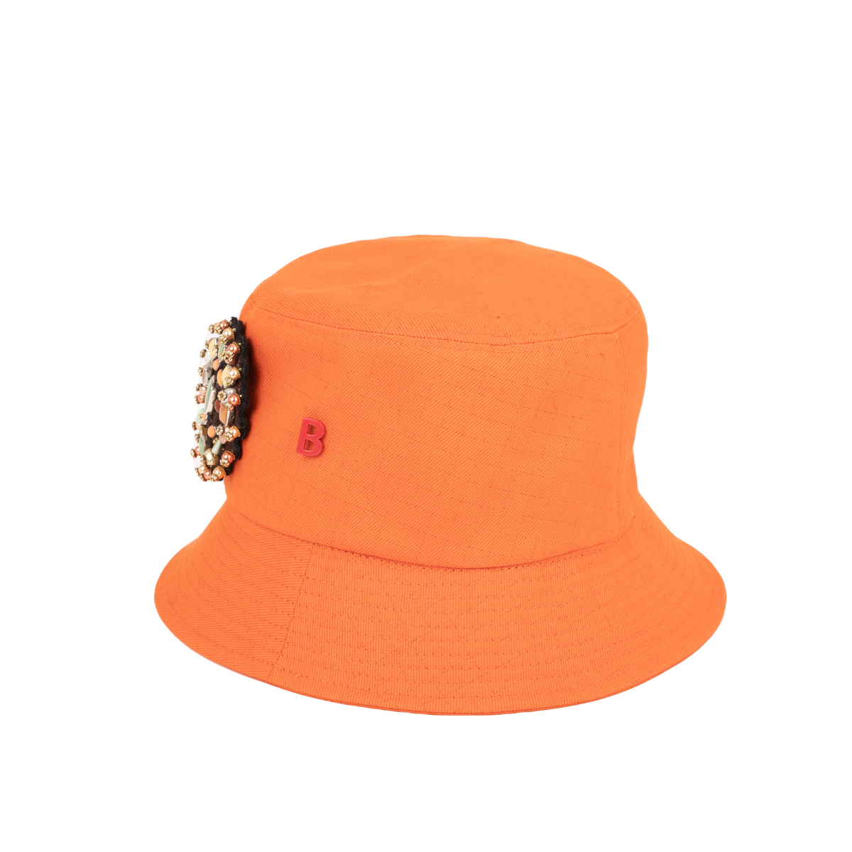 An orange cotton bucket hat with an embroidered brooch representing a yourte pinned on it. 